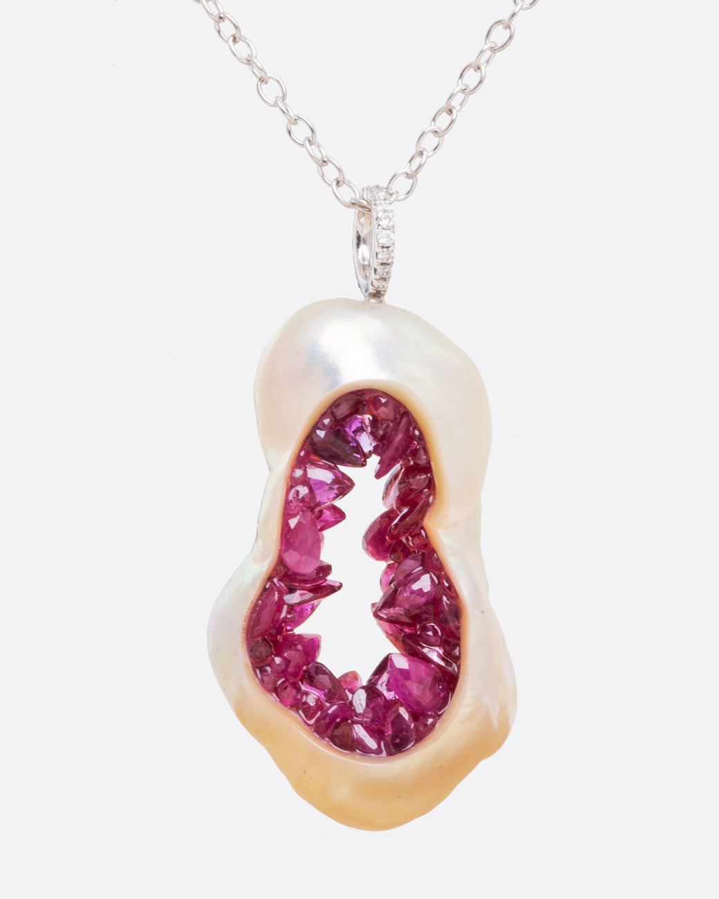 A large soufflé pearl open in the center and filled with pearls and amethysts, hanging from a white gold cable chain and a diamond bail. Shown from the front.
