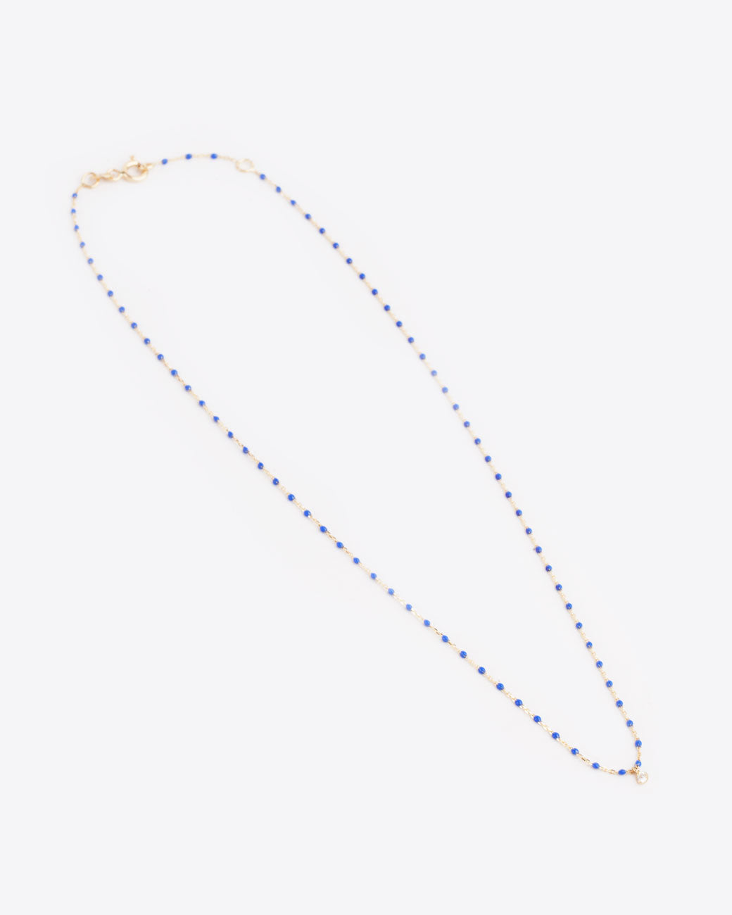 A yellow gold cable chain necklace with droplets of blue resin and a single diamond charm. Shown diagonally from the front with the clasp closed.