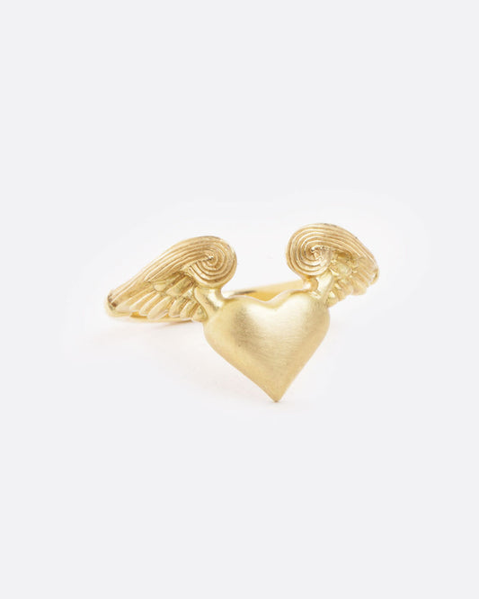 A yellow gold ring with a heart with wings on it. Shown from the front.