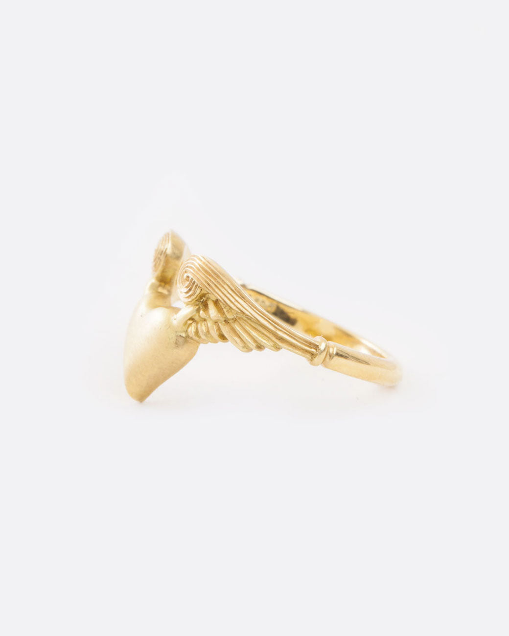 A yellow gold ring with a heart with wings on it. Shown from the side.