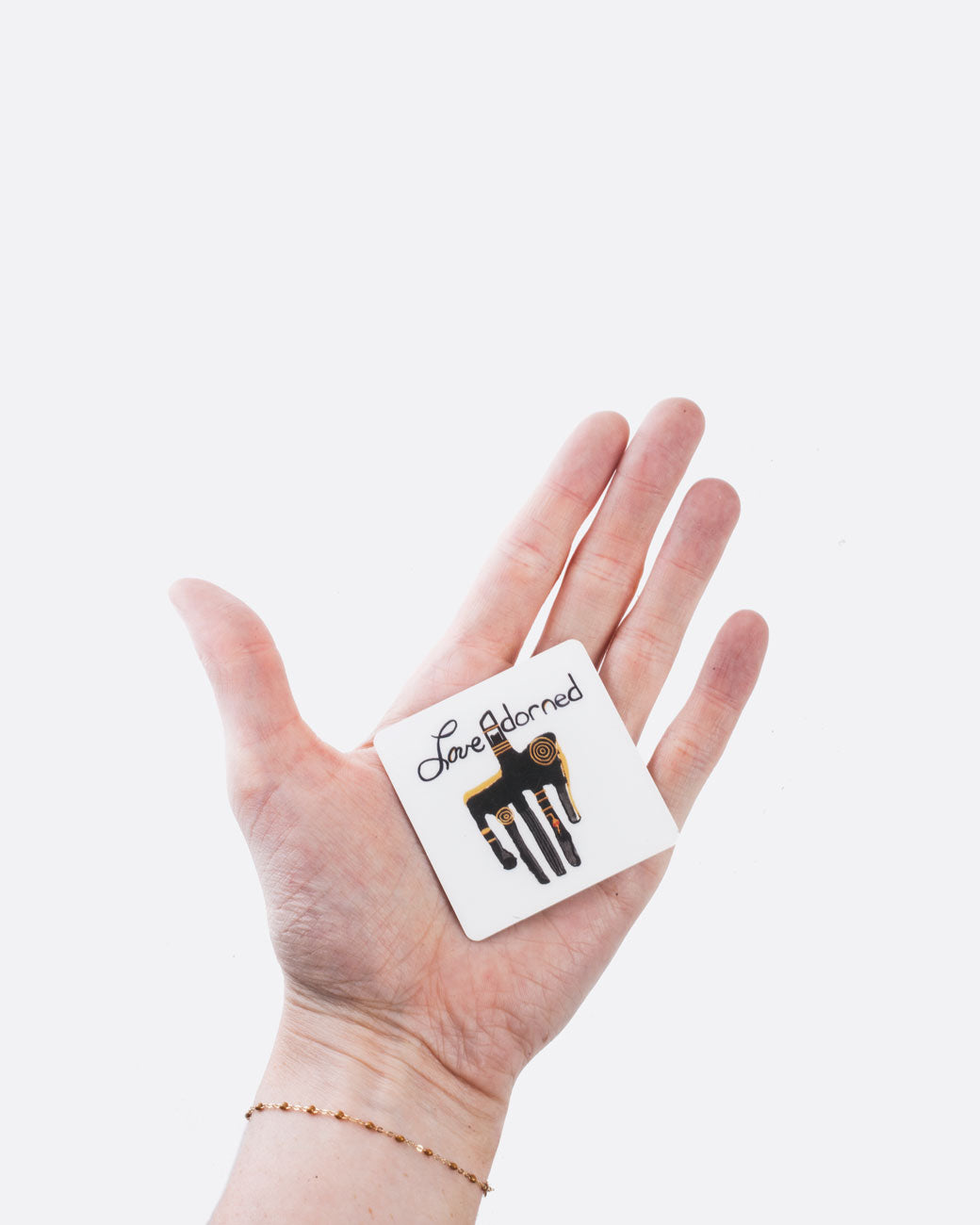 A square two inch gift card printed with a custom painting by love adorned founder of a primitive hand and the love adorned logo. Shown from the front in a hand.