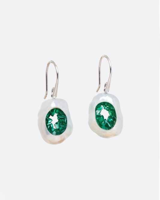 A pair of dangle earrings with hollow pearls lined with emeralds and white gold ear hooks. Shown from the front.