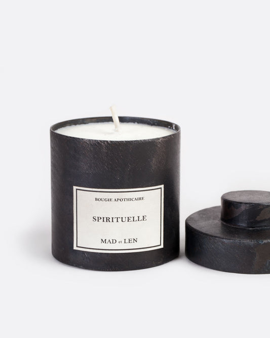 A Mad et Len Spirituelle candle measuring 3" tall and 3.25" wide. It is housed in a blackened iron vessel and has a label that reads: Bougie Apothicaire Spirituelle Mad et Len. Shown open from the front with its lid on the side.