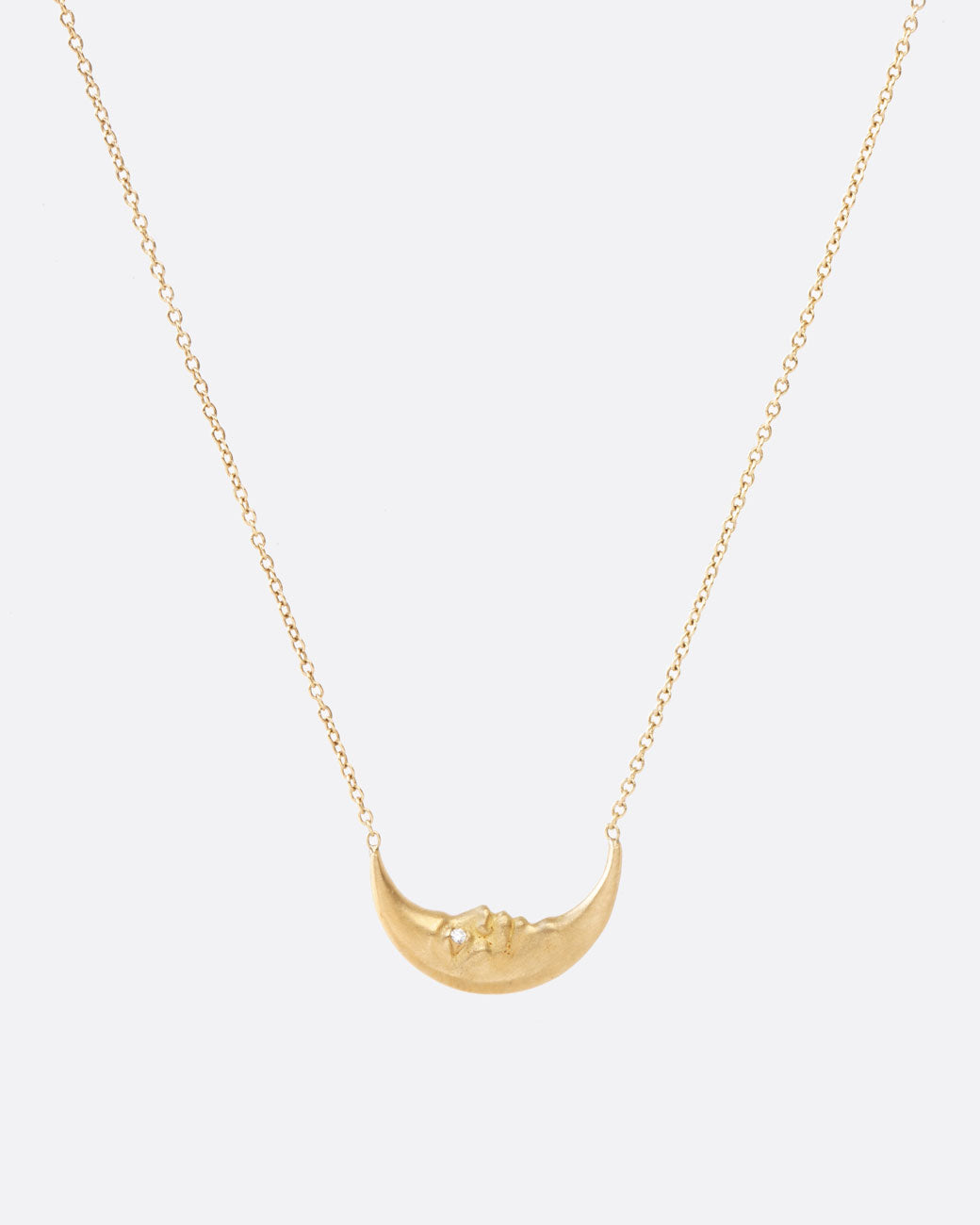 A yellow gold crescent moon pendant necklace with a carved face and diamond eyes. Shown from the front.