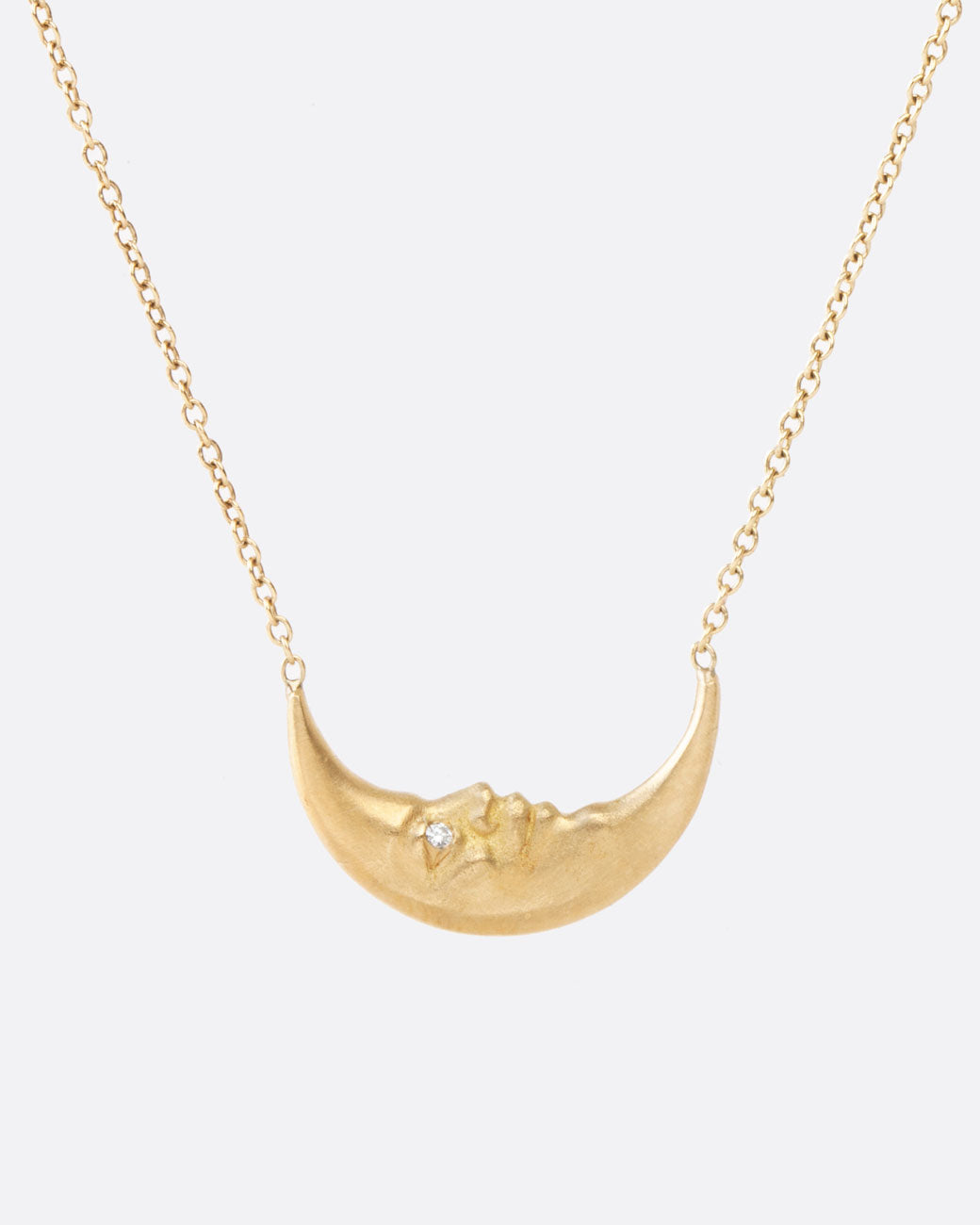 A yellow gold crescent moon pendant necklace with a carved face and diamond eyes. Shown from the front.