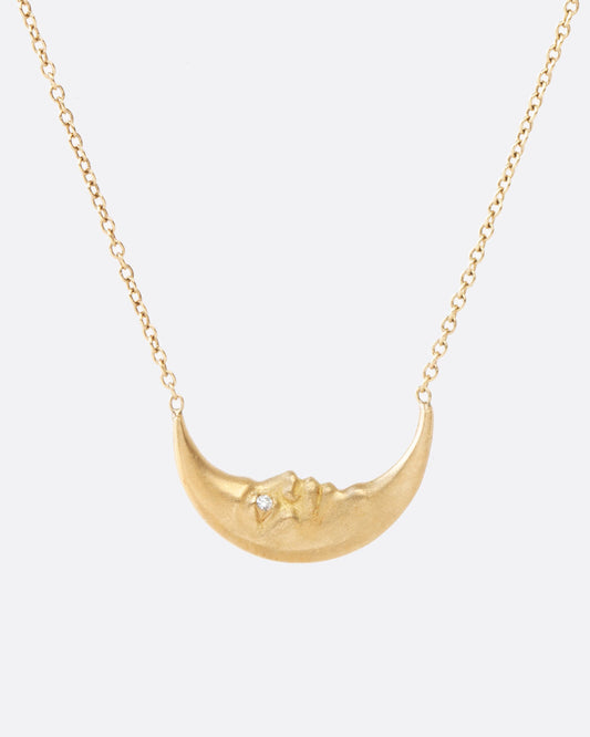 A yellow gold crescent moon pendant necklace with a carved face and diamond eyes. Shown from the front.