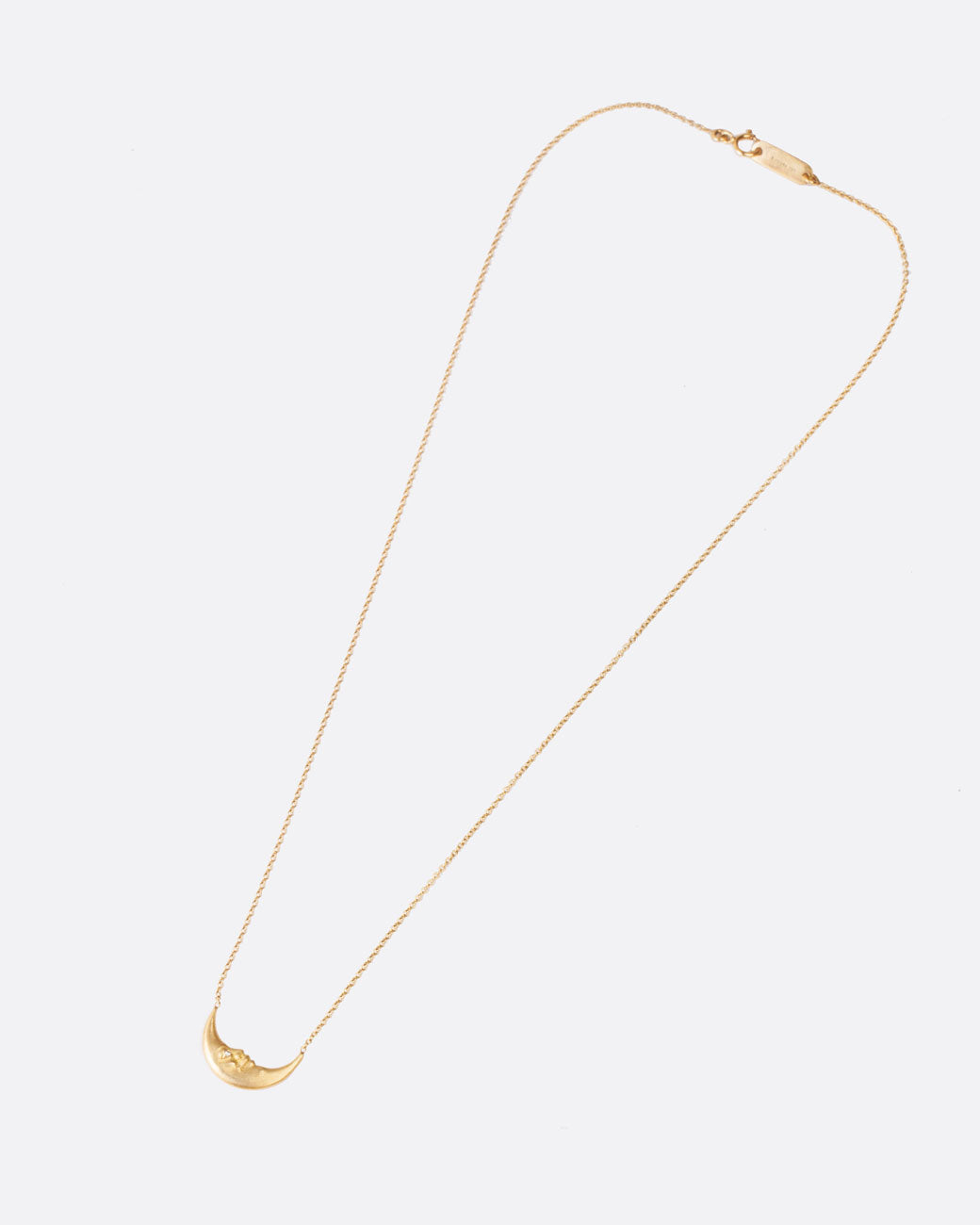 A yellow gold crescent moon pendant necklace with a carved face and diamond eyes. Shown closed lying on its side from the front.