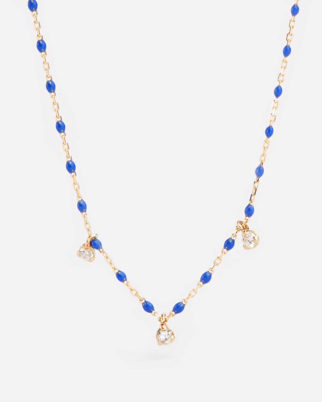 A yellow gold cable chain necklace with droplets of blue resin with three diamond charms. Shown from the front.