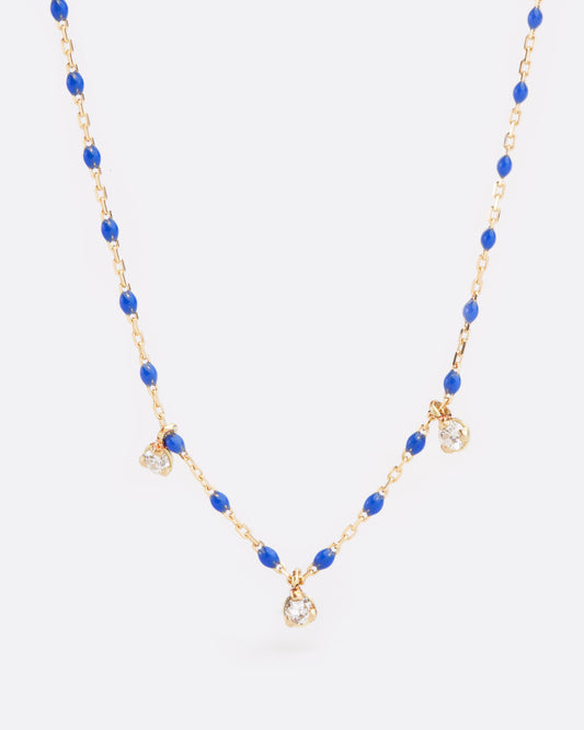 A yellow gold cable chain necklace with droplets of blue resin with three diamond charms. Shown from the front.
