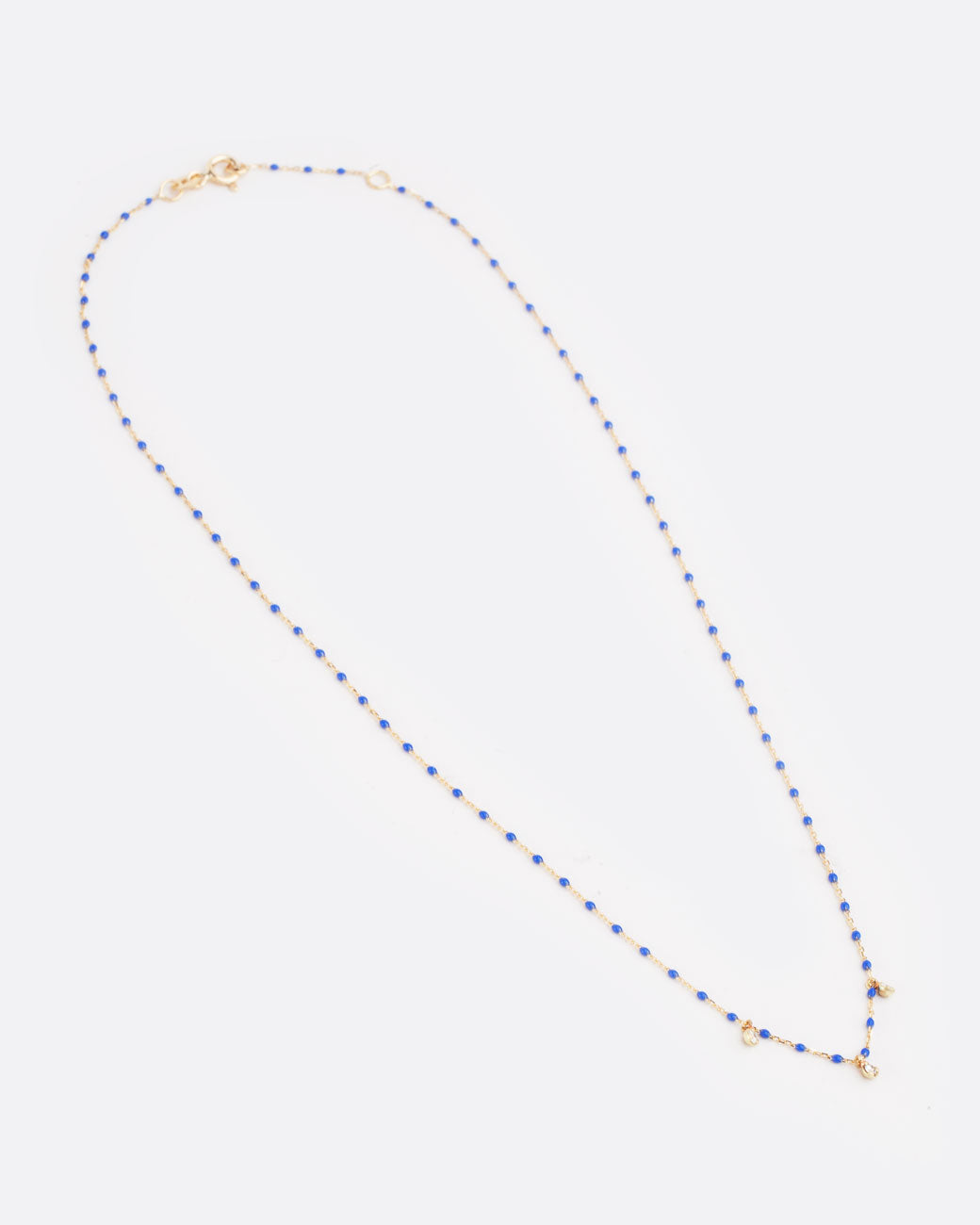 A yellow gold cable chain necklace with droplets of blue resin and three diamond charms. Shown diagonally from the front with the clasp closed.