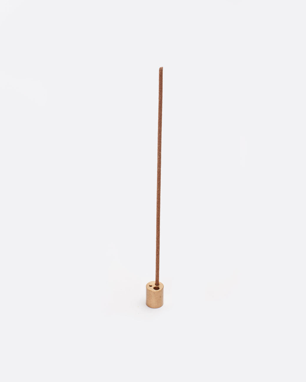 A brass incense stand with three different size holes on the top and a single incense stick in one. Shown from the front. 