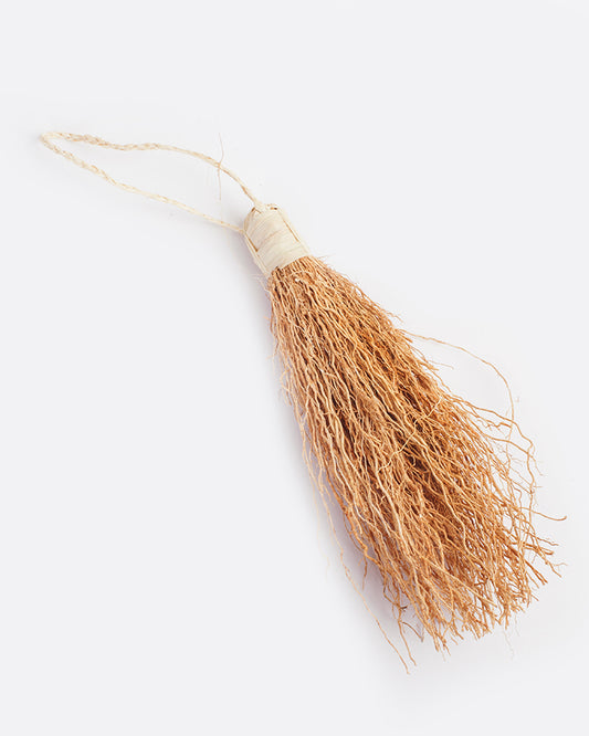 A tassel of vetiver root wound tightly on one end with twine that forms a loop for hanging. The vetiver is natural light honey color and twine is an off white. Shown lying flat from the side.