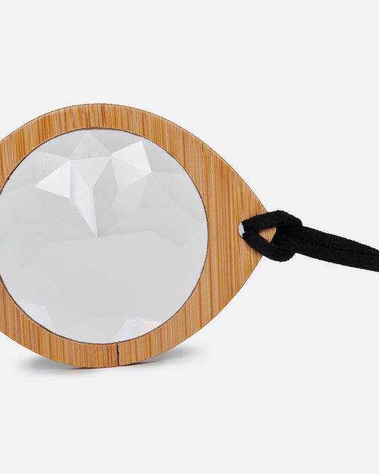 A bamboo monocle on a suede cord. Shown standing up on its side from the front.