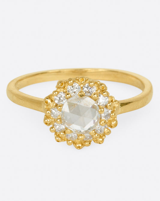 A yellow gold rose cut round diamond ring with a halo of smaller round brilliant cut diamonds shown from the front.