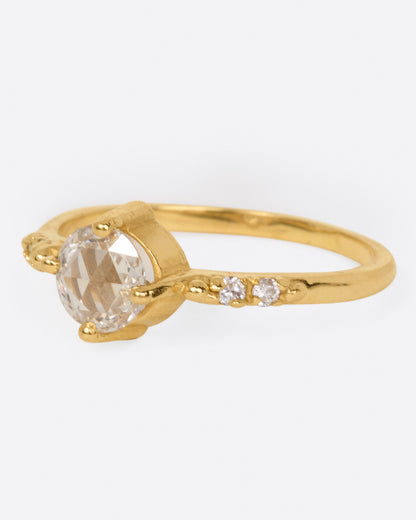 A yellow gold ring with a prong set rose cut diamond at the center and two diamonds on either side, shown from the side.