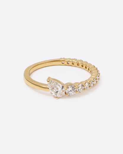 A yellow gold ring with graduated white diamonds halfway around and one pear shaped white diamond at its center shown from the front.