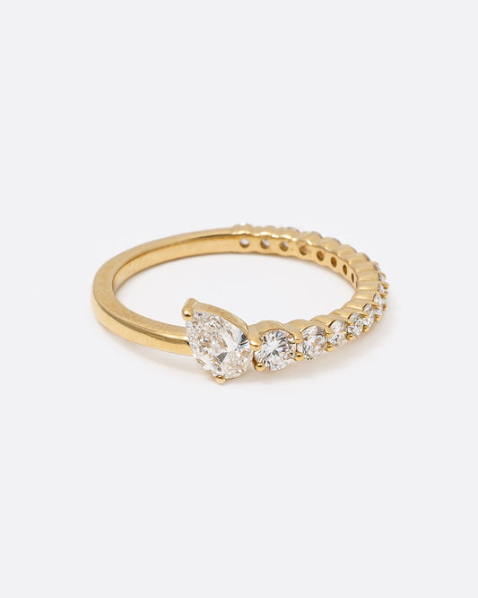 14k yellow gold ring with graduated white diamonds halfway around and one pear shaped white diamond by Selin Kent, shown from the front.