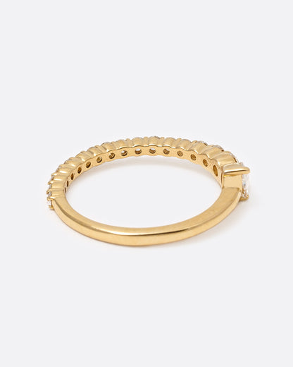 A yellow gold ring with graduated white diamonds halfway around and one pear shaped white diamond at its center, shown from the side.