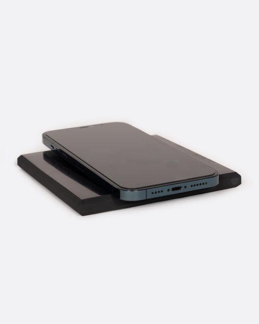 A black stone tile with a cell phone lying on top. Shown lying flat at an angle.