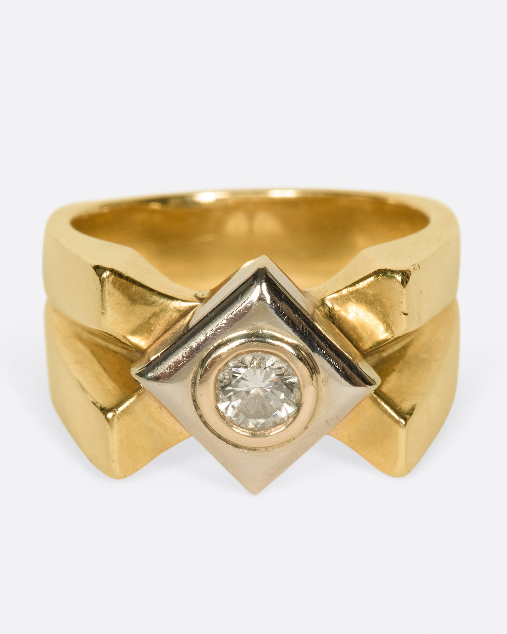A heavy, gold, X-shaped ring with a white gold square and a round diamond at its center.
