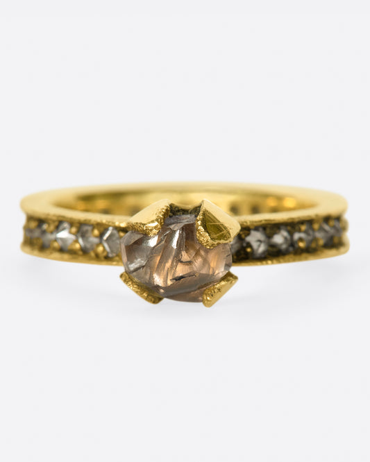 A yellow gold eternity band with inverted diamonds, crowned by a prong set raw yellow diamond. Shown from the front.