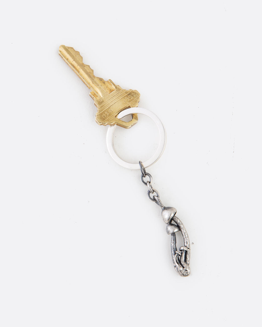 A silver keychain with a cluster of mushrooms and a key attached to the ring. Shown lying flat from the front.