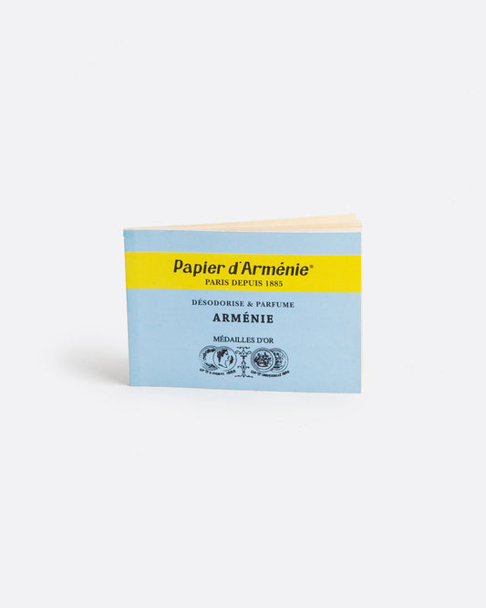 A light blue and yellow booklet of paper incense. The front reads: 'Paper d'Arménie PARIS DEPUIS 1885 DÉSODORISE & PARFUME ARMÉNIE MÉDAILLE D'OR' and has medallion imagery at the bottom. Shown standing up from the front.