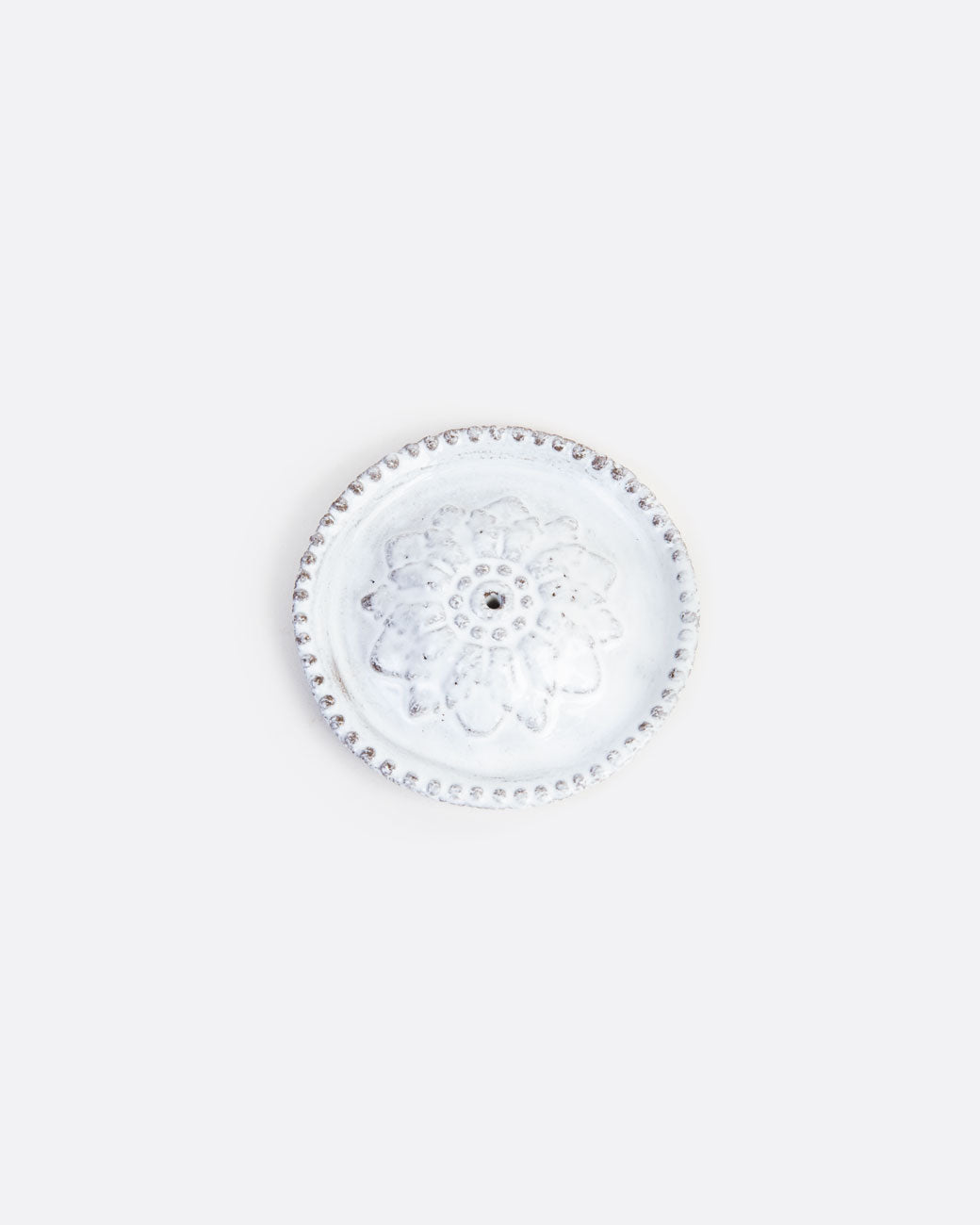 A round white ceramic incense holder with a flower at its center and a hole for  incense. Shown from the top.