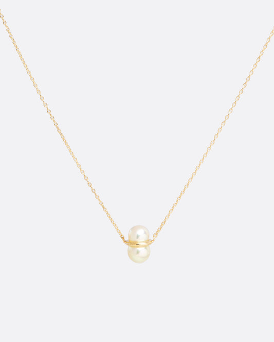 two pearls sit vertically stacked and connected by a gold setting. attached to a thin gold chain to make into a necklace.