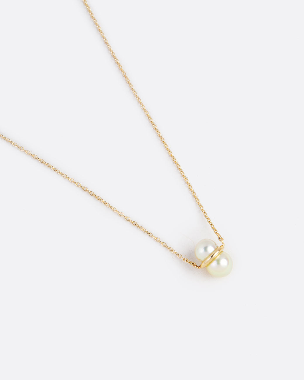 two pearls sit vertically stacked and connected by a gold setting. attached to a thin gold chain to make into a necklace.