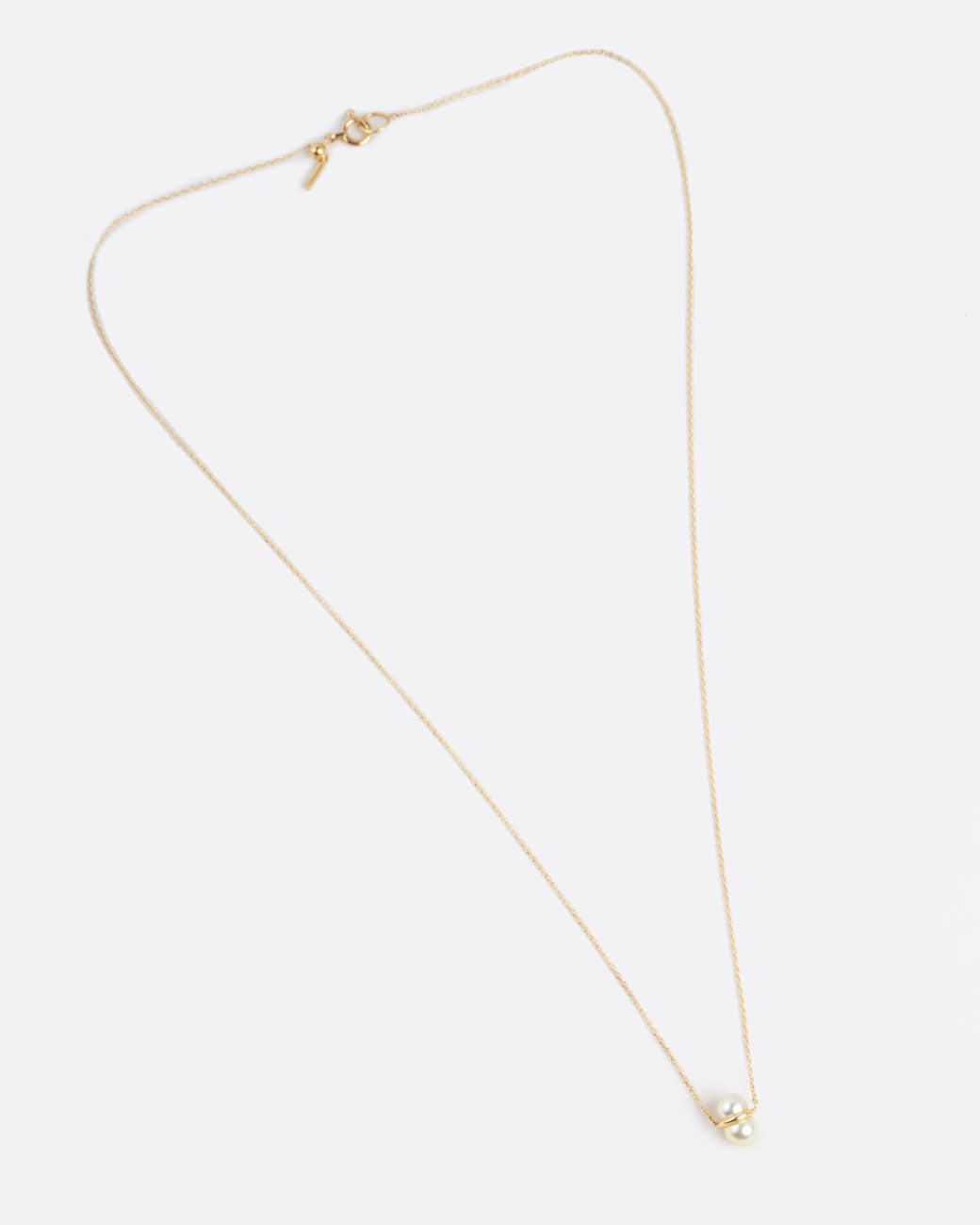 two pearls sit vertically stacked and connected by a gold setting. attached to a thin gold chain to make into a necklace.