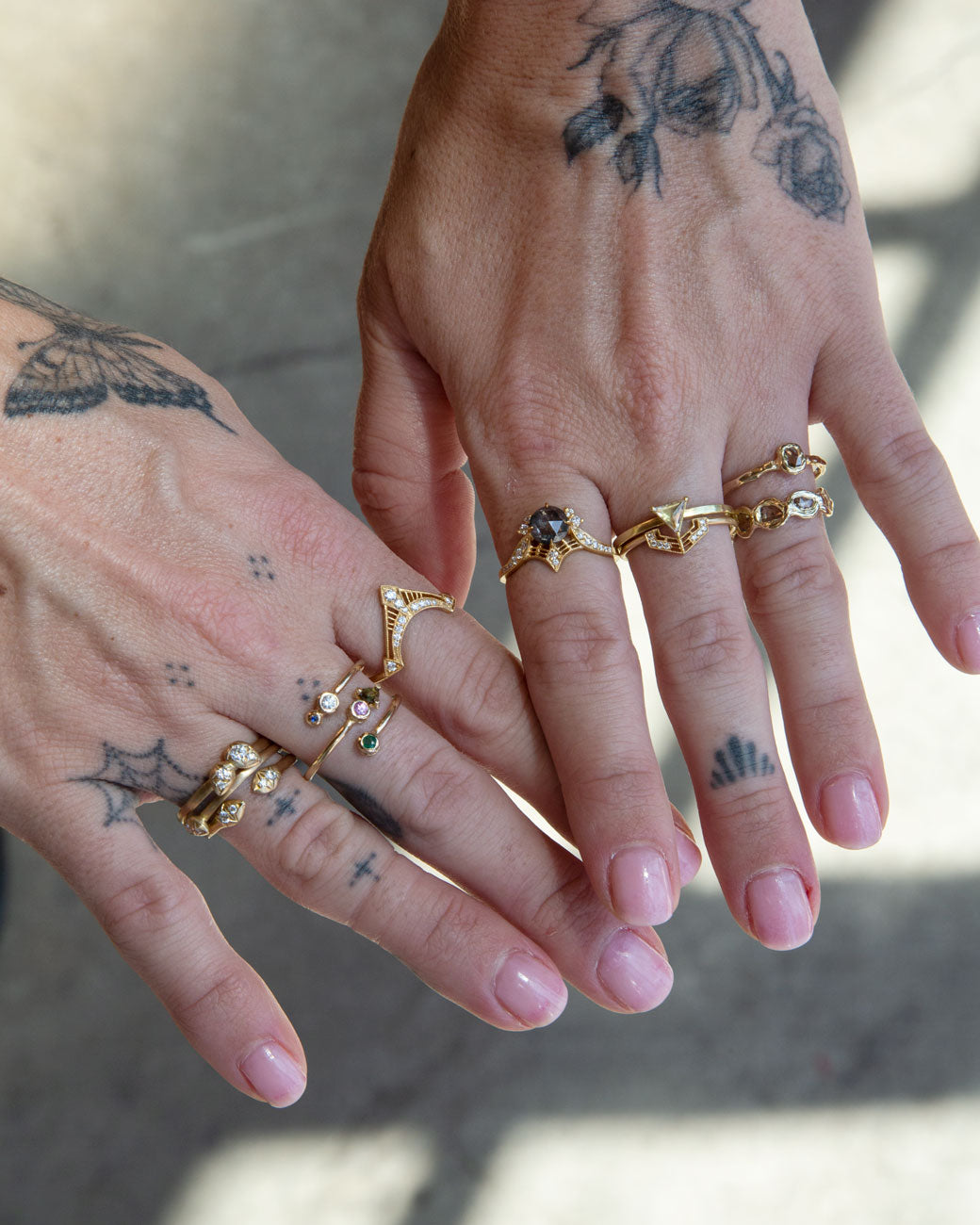 A woman's hands with tattoos and stacked rings on six fingers. Shown from the top.