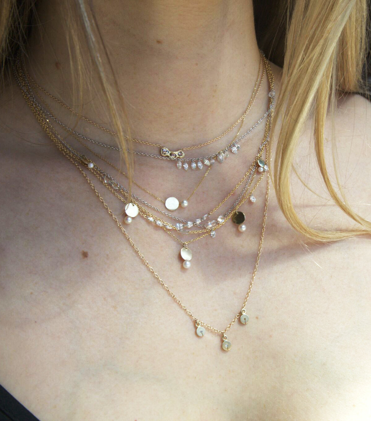 Layered necklaces on a woman's neck. The lowest is a yellow gold cable chain necklace with three disc charms. Each disc has a single gray diamond with a slit in the bottom. Shown from the front.