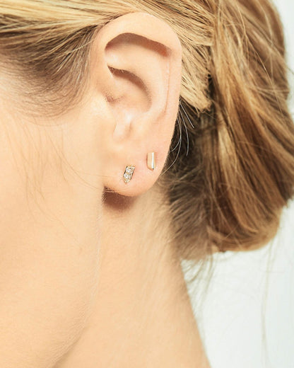 A rose gold stud earring with two angled sides. Shown from the front on an ear above  a diamond stud earring from the front.